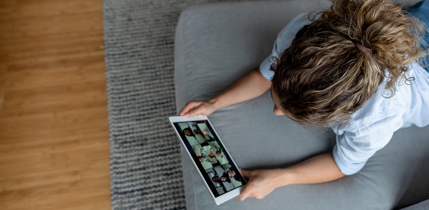 A woman at home in lockdown using her tablet while on the sofa to have a video call with many other people she knows.