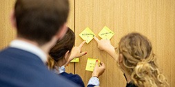 Image of three people completing a group exercise using sticky notes on a wall.
