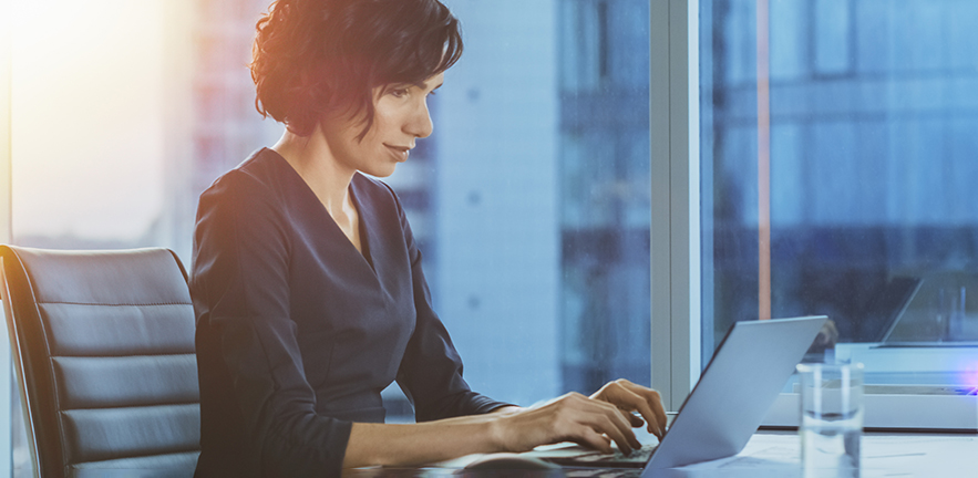 Side view portrait of a businesswoman working on a laptop in a modern office with Cityscape window view.