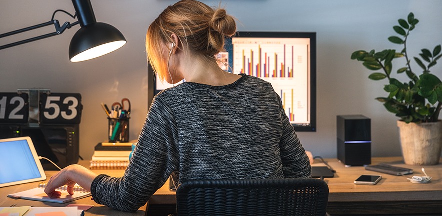 Woman with headphones in focussing while working on computer and digital tablet in her home office during the pandemic.