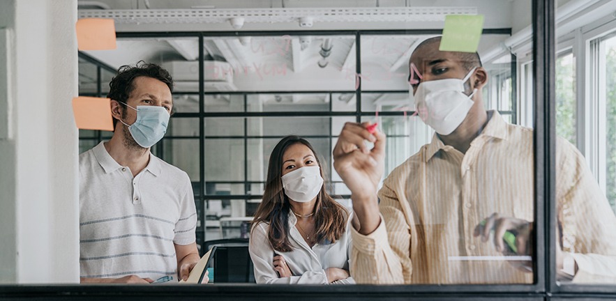 Businesspeople wearing face masks brainstorming in a meeting.