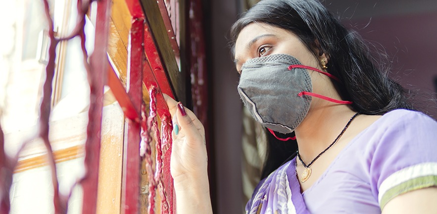 Indian woman gazes out of the window while protecting herself and wearing a mask against the coronavirus.