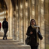 A female student in a scarf walks down a columned path by a College quad.