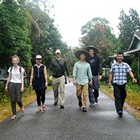 A group of young people, including one of our PhD students, strides down a path in Indonesia smiling at the camera.