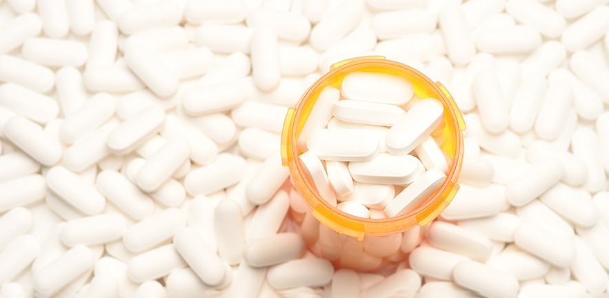High angle view of a prescription bottled filled with pills surrounded by more of the same tablets, with copy space,