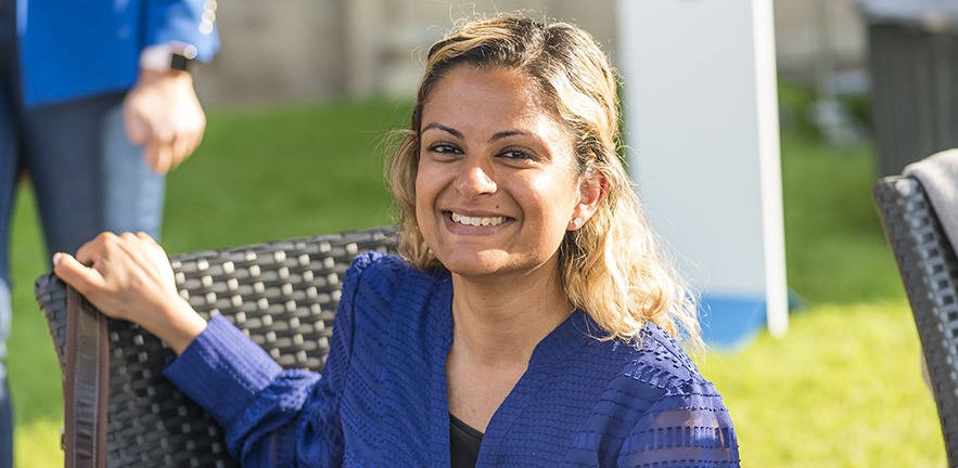 MBA student smiling at the Camera while sitting on a wicker chair on the lawn at an MBA event.