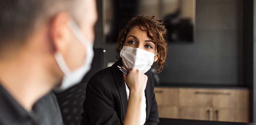 Colleague wearing masks social distancing while in discussion.