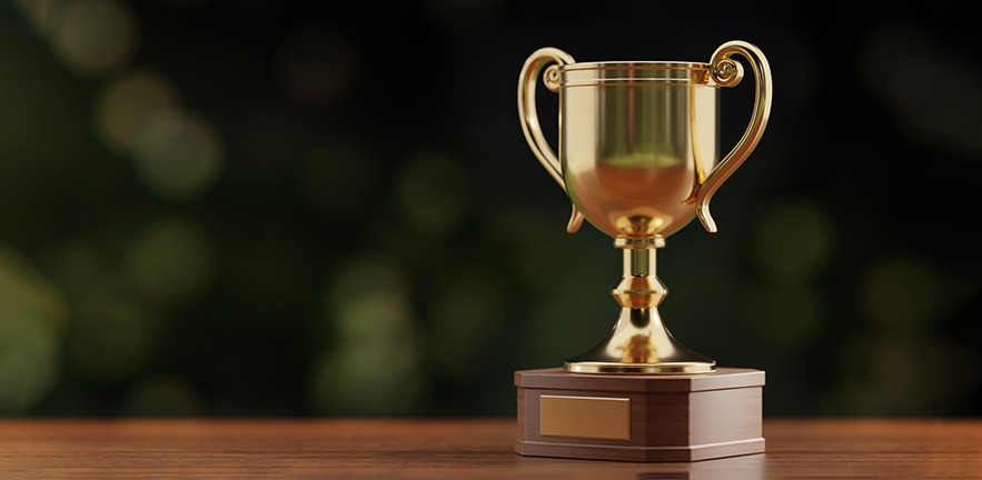 Gold award cup standing on wood surface against green defocused background.