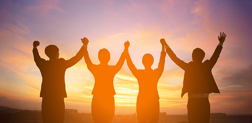 Group of four people silhouetted against the sunset. They have their hands raised in celebration.