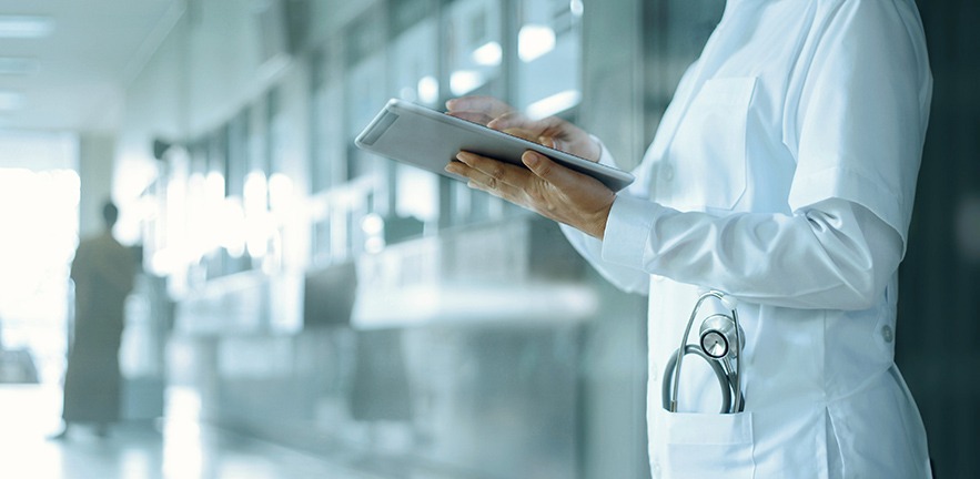 Doctor working on digital tablet while standing in a hospital corridor.