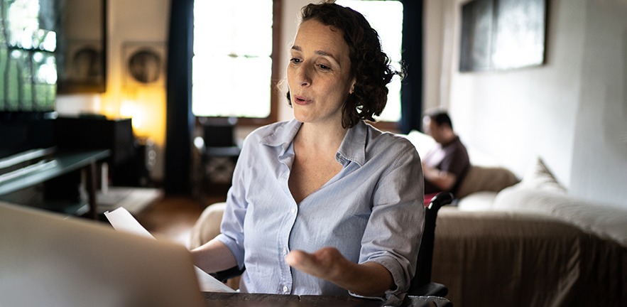 Woman with disabilities doing a virtual business meeting at home. Partner in soft focus sitting in the background.