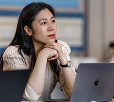 Woman with dark hair in front of a laptop listening to a lecture.