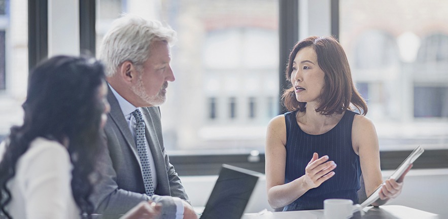 Businesswoman discussing with colleagues who are sitting at a table in a boardroom. She is showcasing information to them.