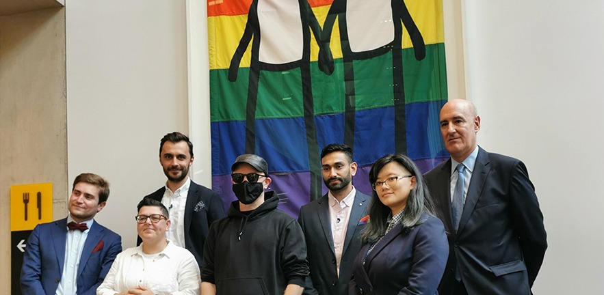 STIK and the event speakers stand in front of the newly unveiled Pride Banner.