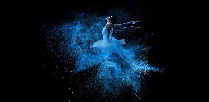 A ballet dancer leaps into a blue powder cloud.