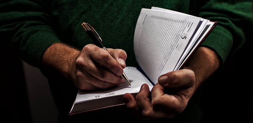 Close up of a man writing in a diary with a pen.