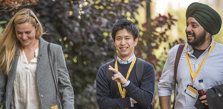 Three MBA students, one female and two male, walking outside in the sunshine.