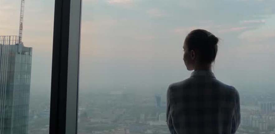 A businesswoman looks out of the window of a skyscraper at the city below.