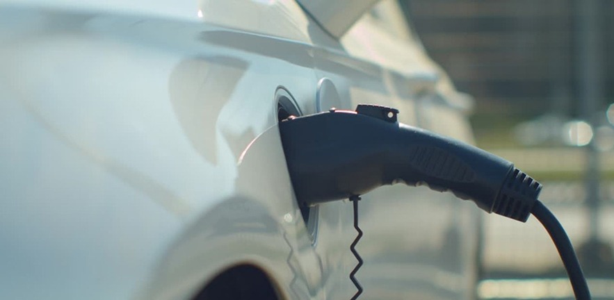 An electric car being charged on a parking lot with a charging station in the city.