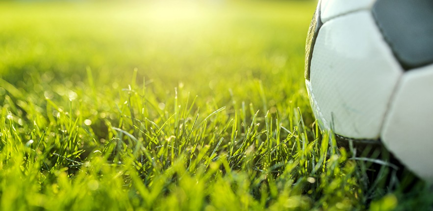 Photo of a traditional football ball on green football field during bright sunny day.