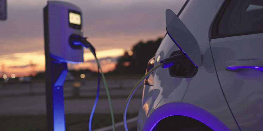Electric car being charged as the sunsets in the sky behind.