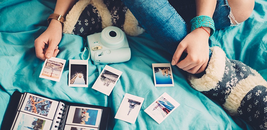 Woman sits on her bed arranging her travel photos.