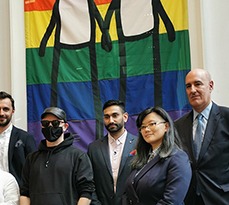 STIK and the event speakers stand in front of the newly unveiled Pride Banner.