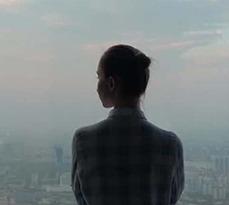 A businesswoman looks out of the window of a skyscraper at the city below.