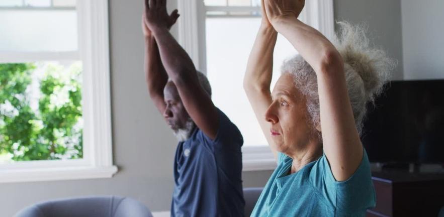 A senior couple practise yoga together in the living room at home.