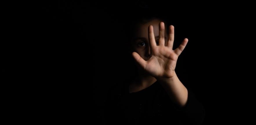 Young girl in shadow with a raised hand making a stop sign gesture on a black background.