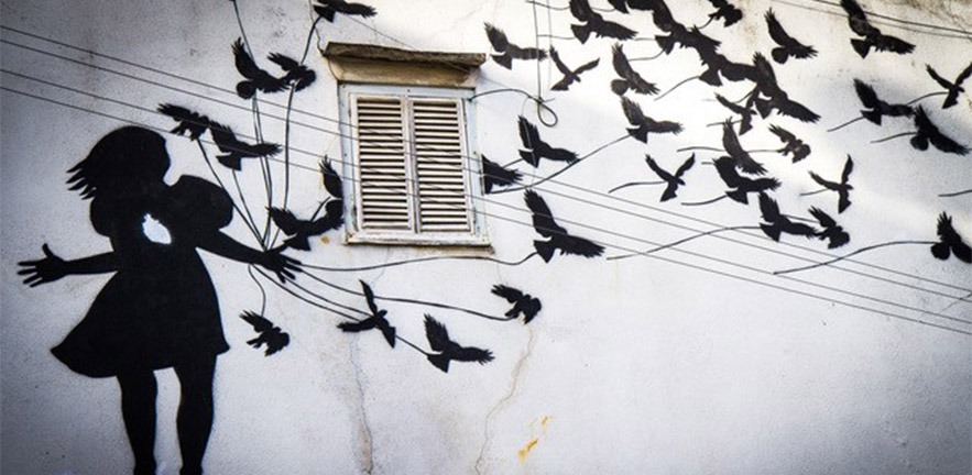 Graffiti art of a girl and a lot of birds in black on a white wall.