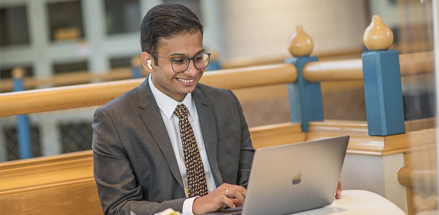 Male MBA student working on a laptop, smiling.