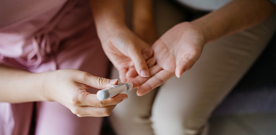 A woman helping another person check their blood sugar level at home.