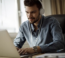 Young man using laptop with headphones on.