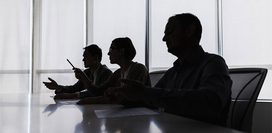 Silhouette of three business people negotiating at a meeting table.