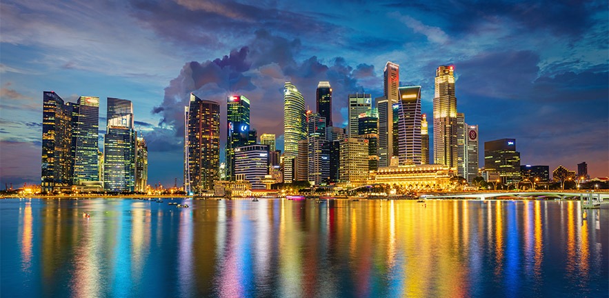 Central business district in Singapore reflected in the water of Marina Bay at dusk.