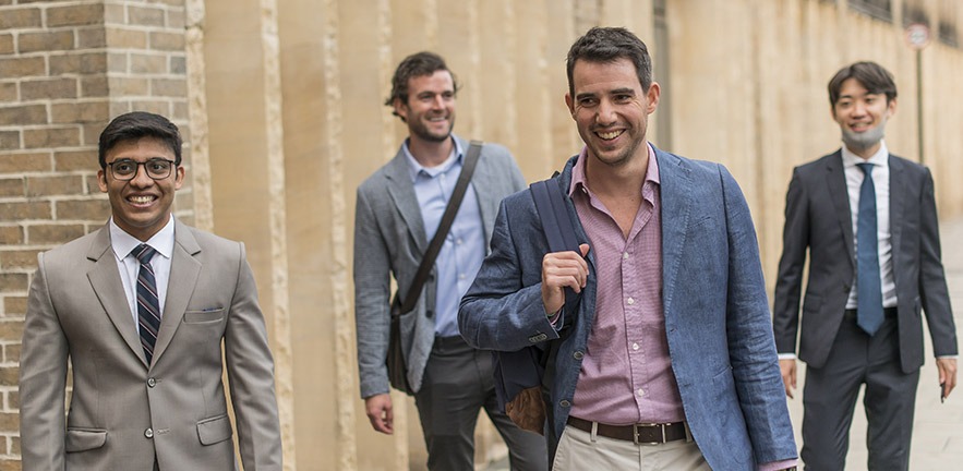 A group of smiling male MBA students outside.