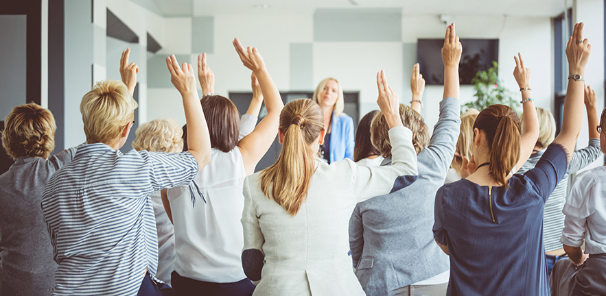 Rear view of business team raising their hands for a vote during a seminar.