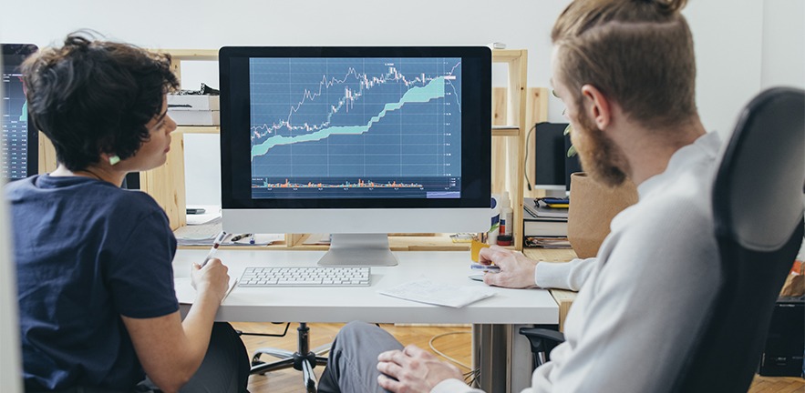 Two colleagues analysing a financial chart on a computer.