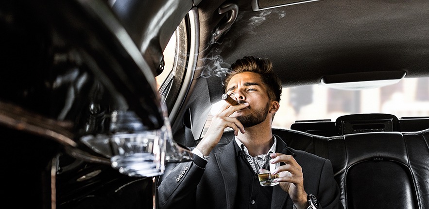 Pensive businessman in a limousine with glass of champagne and smoking cigar.