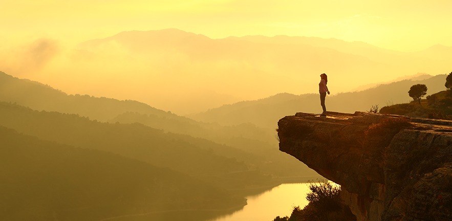 Woman breathing at the top of a cliff at sunrise in the mountains.