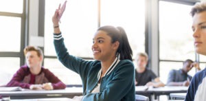 Smiling teenage student raising hand in classroom.