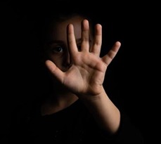 A child in the dark holds up their hand in front of their face.