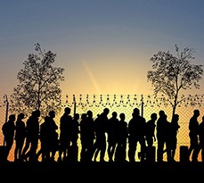 Silhouettes of refugees waiting by a chainlink fence.