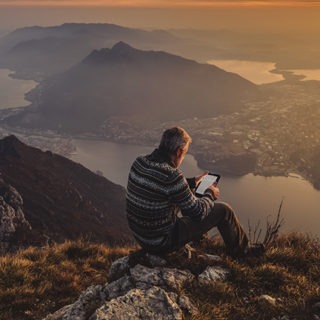 Hiker reading an e-book on a mountain during the golden hour.
