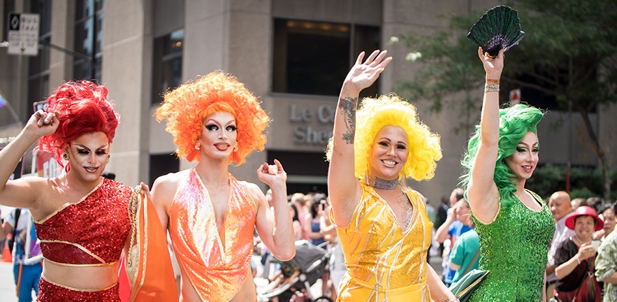 Drag queens wearing red, orange, yellow and green are walking in the street at Montreal Pride.