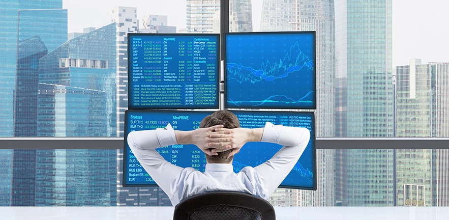 Rear view of a relaxing trader who is sitting in front of a trading station which consists of four screens with financial data.