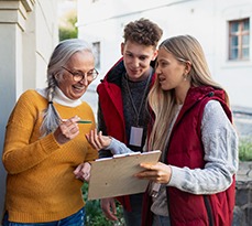 Young door-to-door volunteers talking to senior woman and taking a survey at her front door.