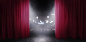 On a stage with red curtains, looking out to the audience.