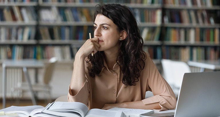 Woman sitting in a library with books and a laptop.